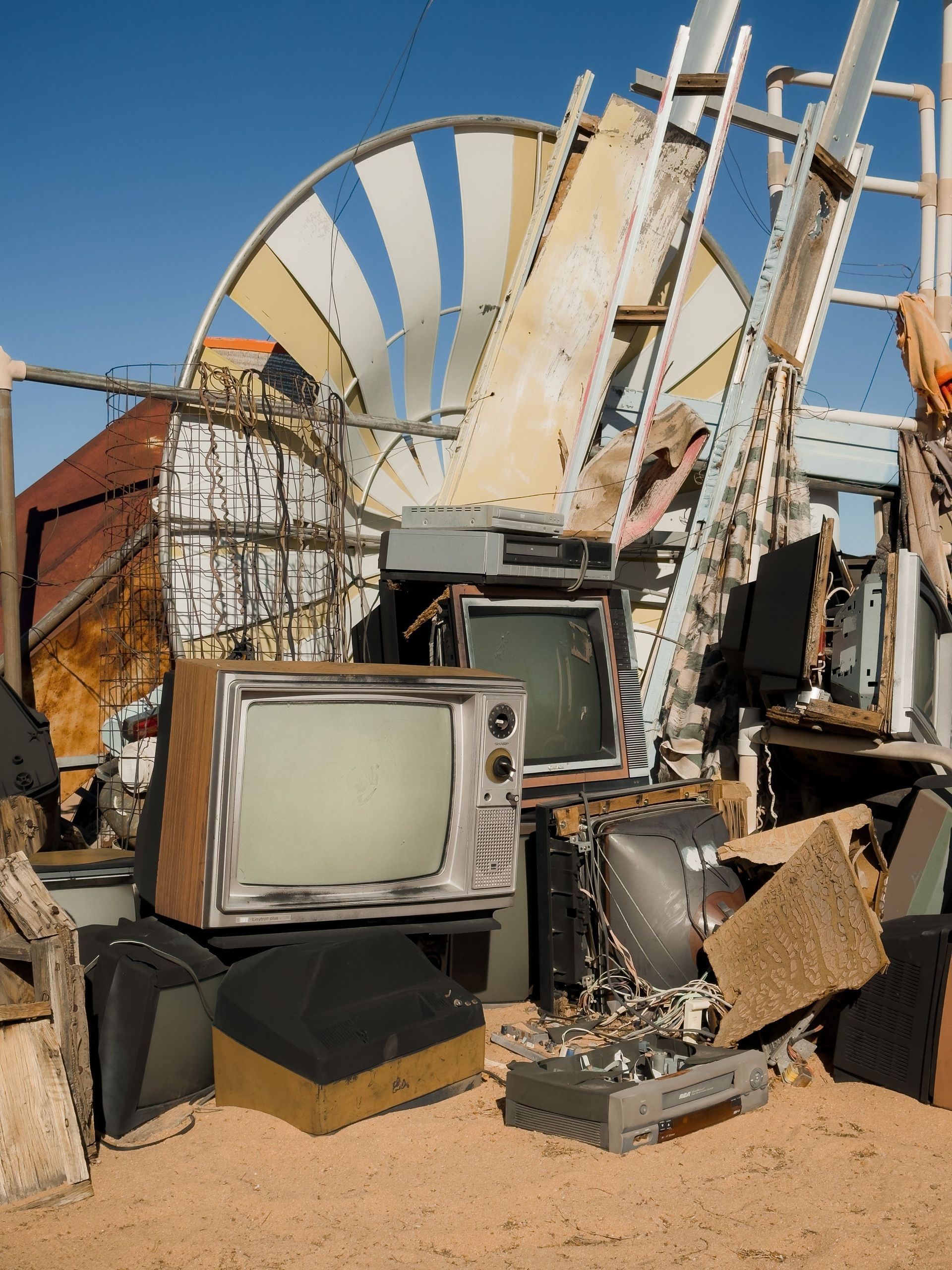 An array of old televisions scattered in the sandy landscape of Joshua Tree junkyard.